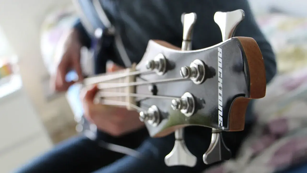Osoba gra na gitarze basowej, tworząc głębokie akordy basowe.