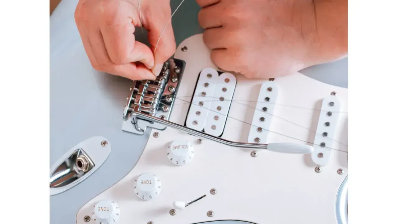 Ręce montują struny do mostka gitary elektrycznej. To ważny krok, jak zrobić gitarę elektryczną, by brzmiała idealnie.