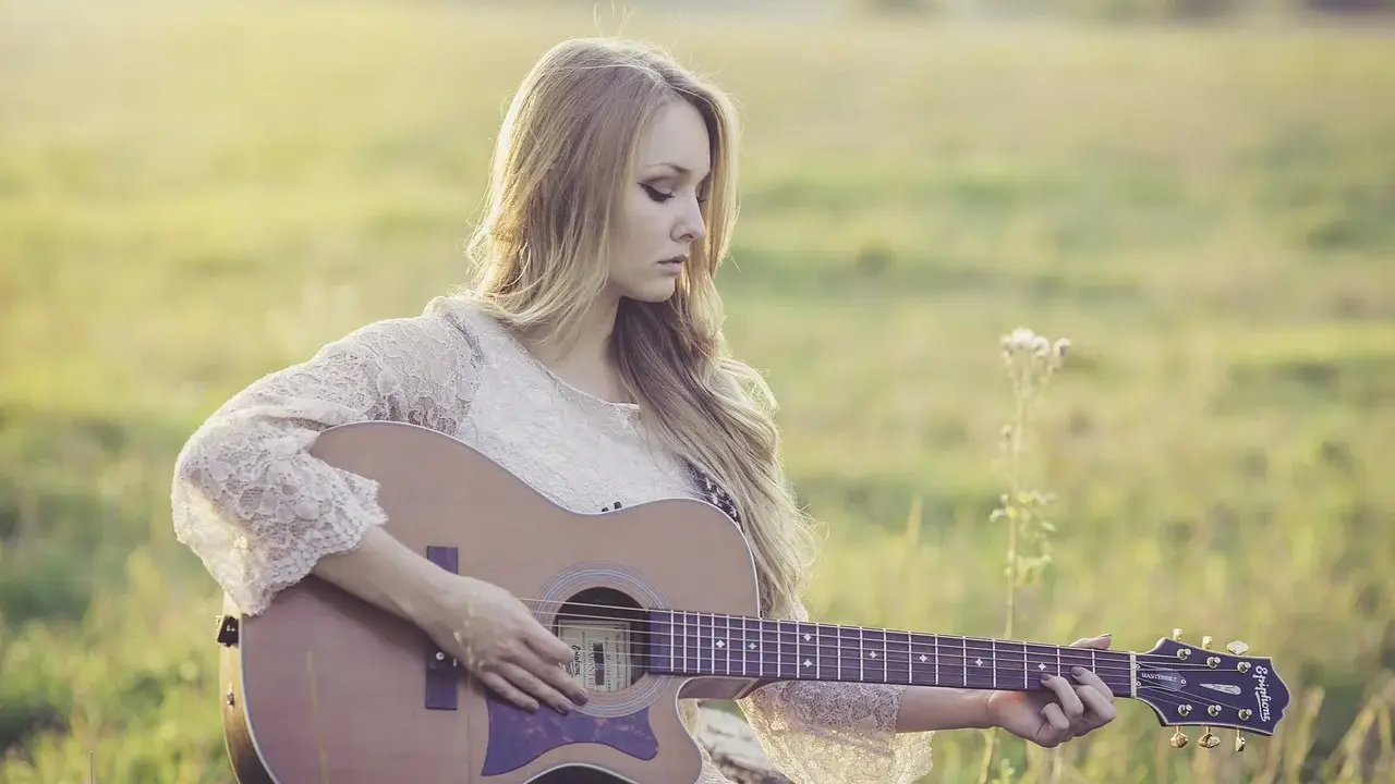 Dziewczyna gra na gitarze, tworząc piękny riff. Słońce delikatnie oświetla jej blond włosy i koronkową sukienkę.