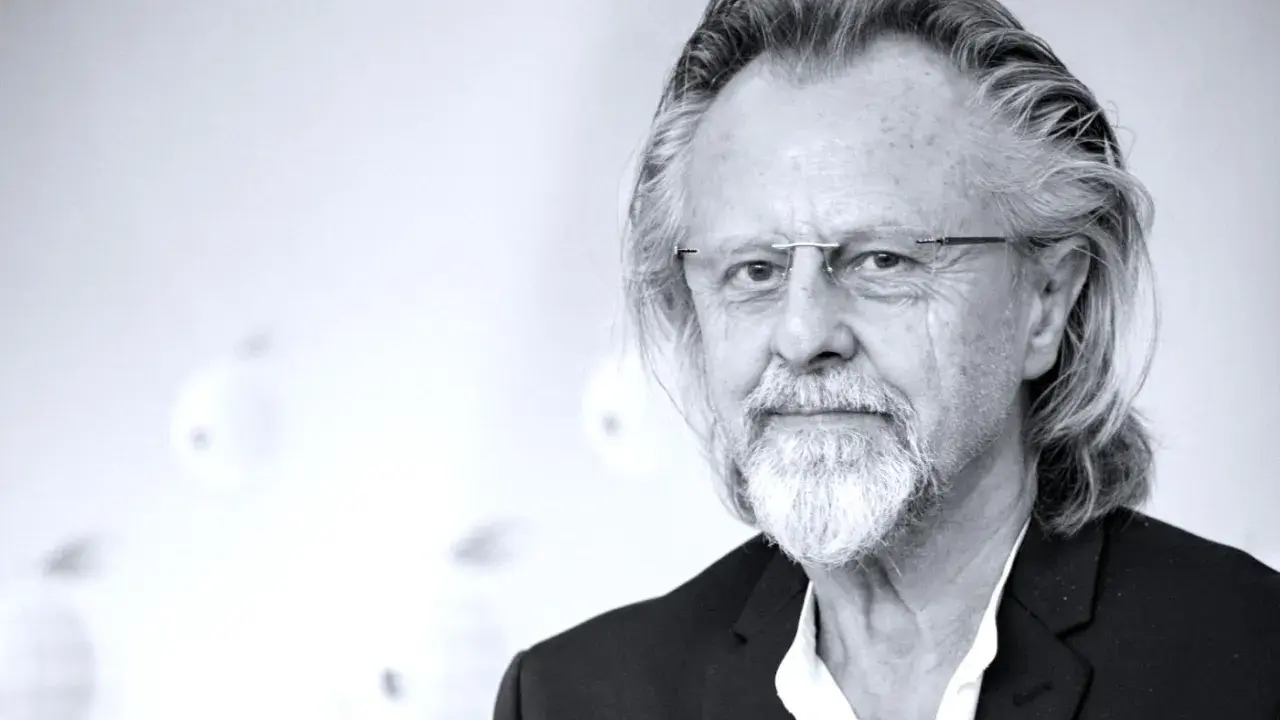 Portret mężczyzny z siwą brodą i długimi włosami, w okularach. Jeden z najlepsi współcześni kompozytorzy.