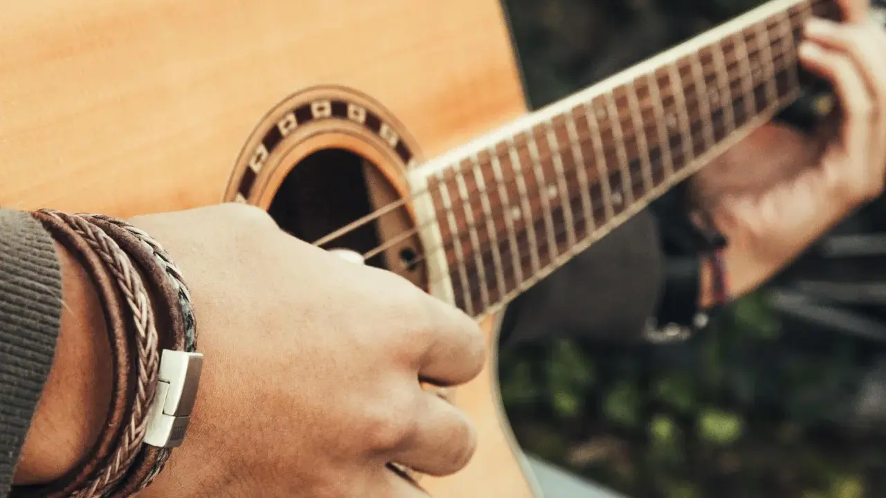 Dłoń z bransoletką z plecionej skóry gra na gitarze akustycznej.