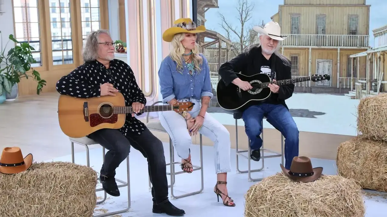 Trzech muzyków gra na gitarach, tworząc muzykę country. W tle stylizowana scenografia z Dzikiego Zachodu.