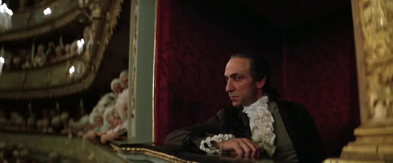 Scena z filmu o Mozarcie. Mężczyzna w stroju z epoki, w loży teatralnej, z widownią w tle.