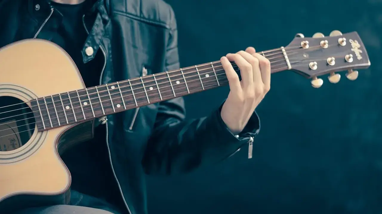 Mężczyzna w skórzanej kurtce gra na gitarze. Akordy układają się w piękną tonację d dur, tworząc melodyjną opowieść.