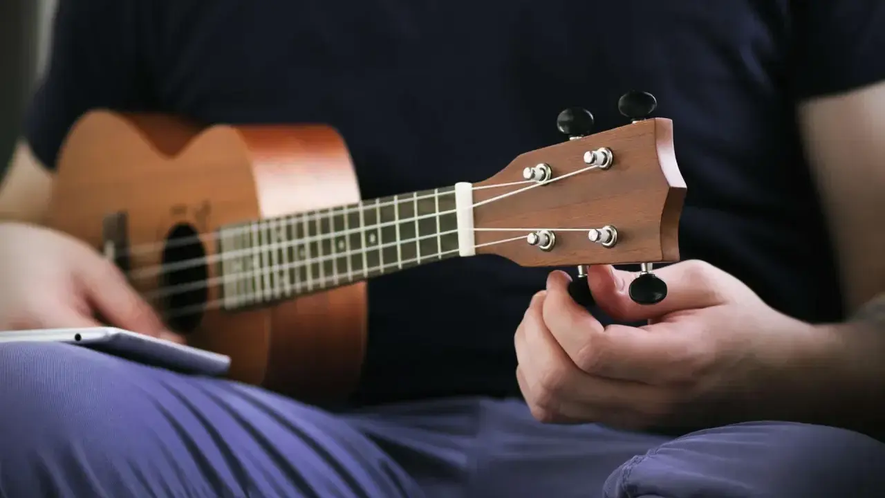 Osoba stroi ukulele, korzystając z aplikacji do nauki gry.