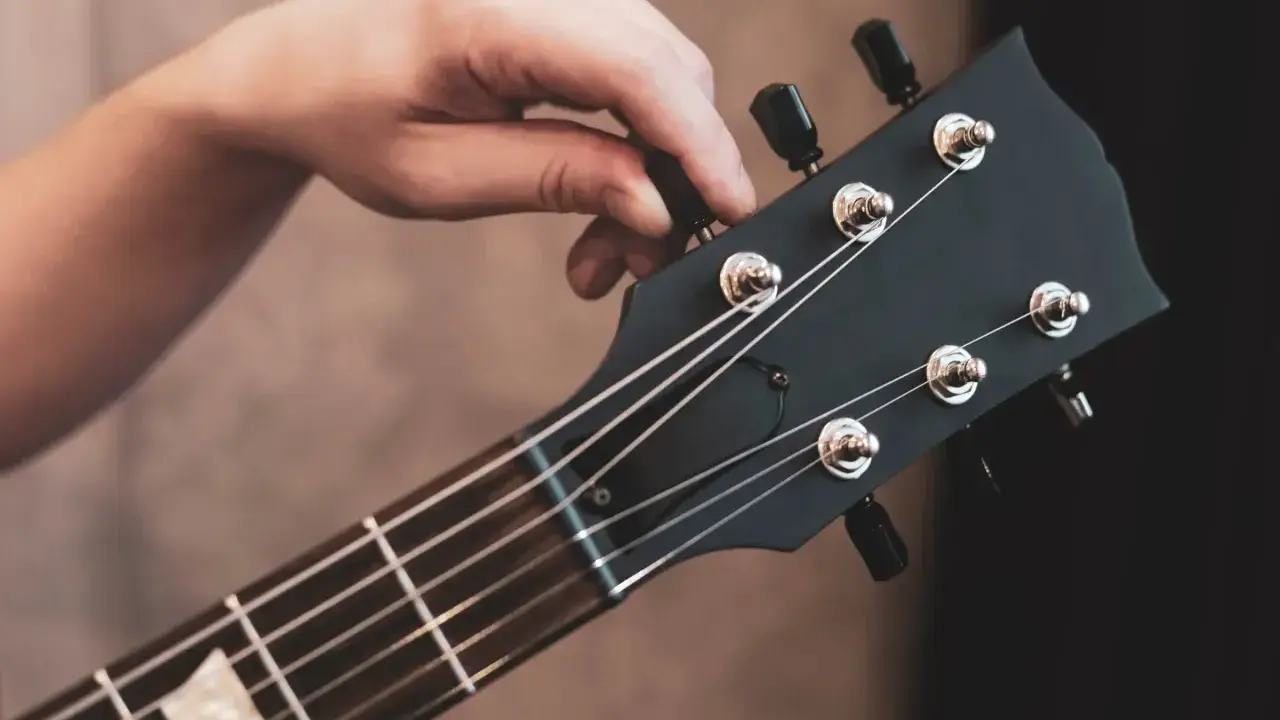 Dłoń kręci kluczem, by nastroić gitarę klasyczną. Idealne brzmienie czeka!