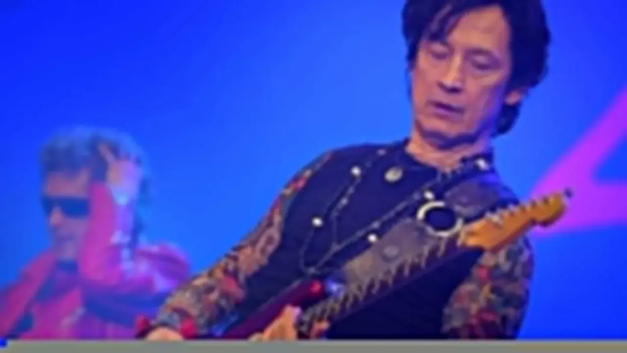 Jan Borysewicz gra na czerwonej gitarze elektrycznej, jego rękawy zdobią tatuaże.