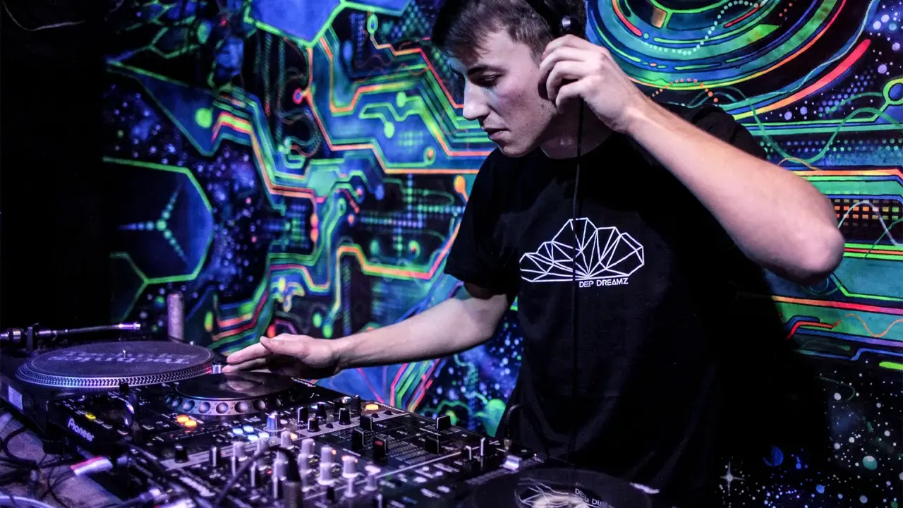 Młody DJ w słuchawkach miksuje muzykę na tle psychodelicznej, neonowej ściany. Chcesz wiedzieć, jak zostać DJ-em? Zacznij od tego!