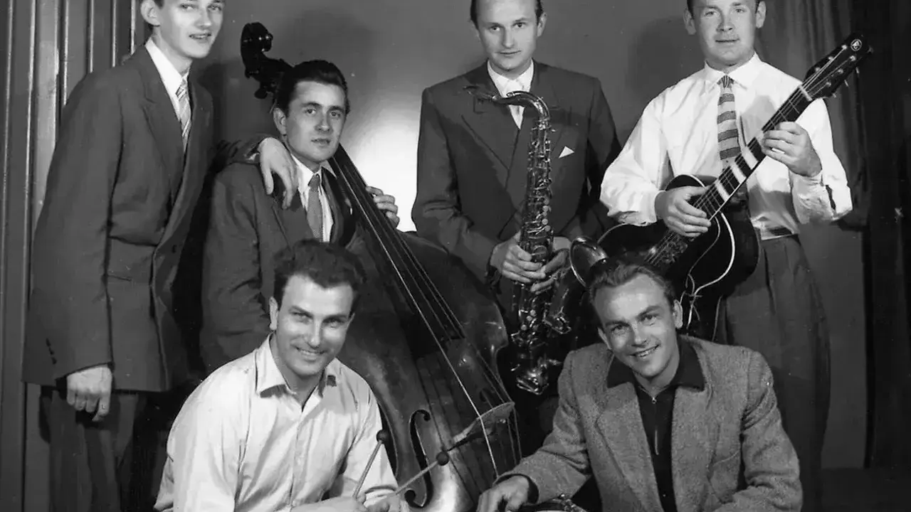 Zespół młodych muzyków, być może najsłynniejsi przedstawiciele jazzu, pozuje z instrumentami: kontrabasem, saksofonem, gitarą i perkusją.