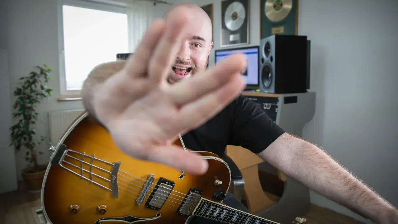 Muzyk z gitarą jazzową, z ręką na pierwszym planie, śpiewa, wyjaśniając, akord co to.