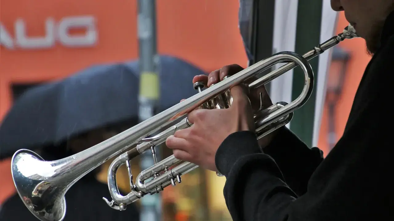 Muzyk gra na trąbce, tworząc dźwięki blues muzyka. W tle deszcz i parasol.