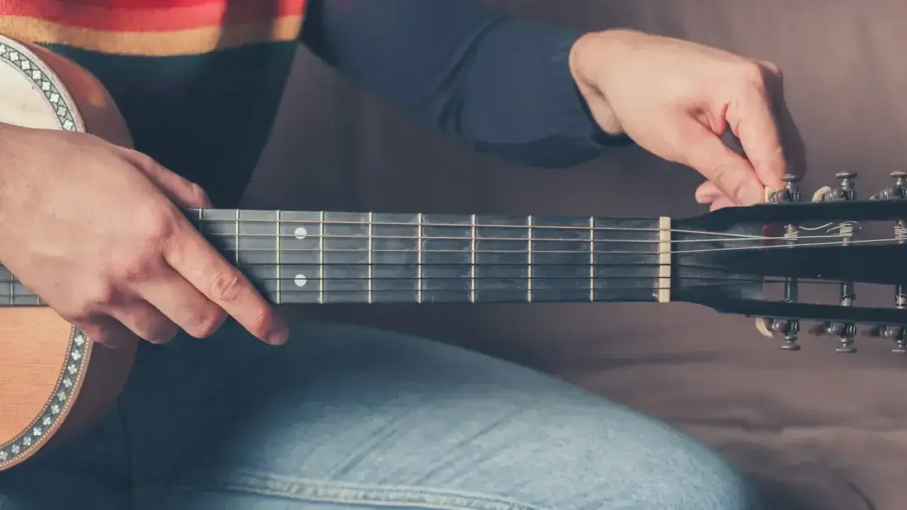 Mężczyzna stroi gitarę 12 strunową, kręcąc kluczem przy główce instrumentu.