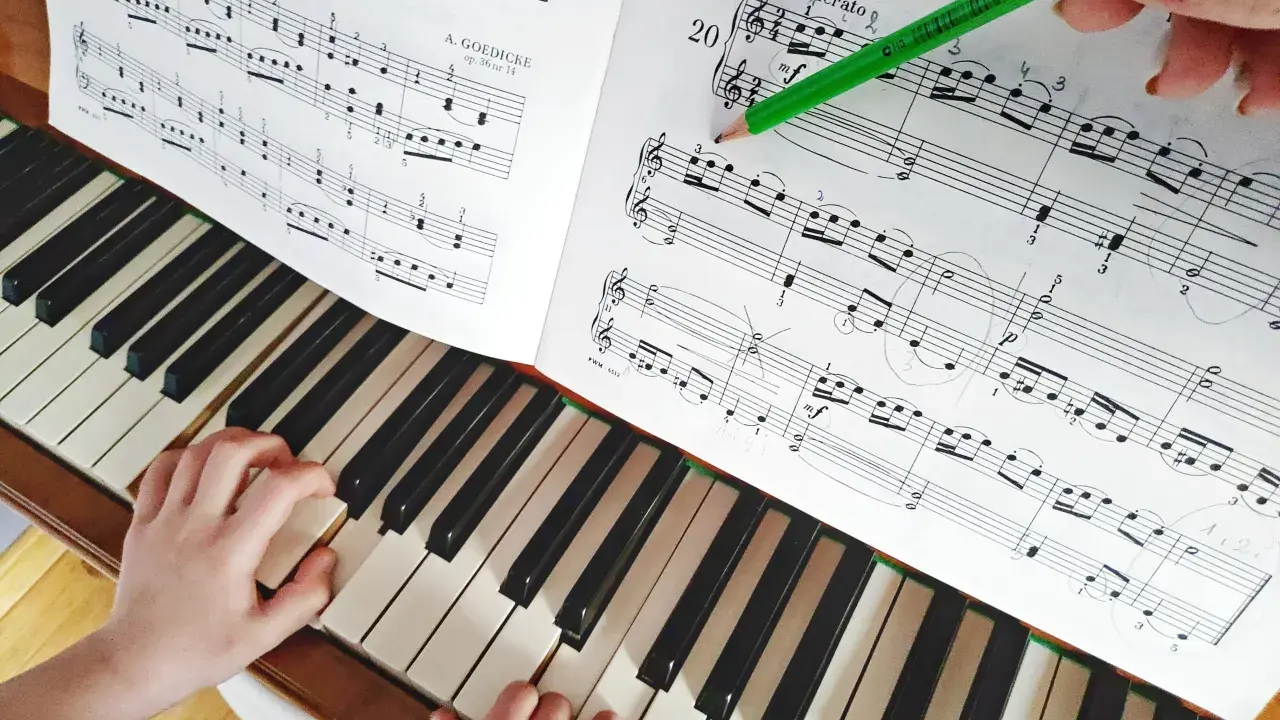 Dziecko uczy się grać na pianinie, ćwicząc nuty z podręcznika. Zielony ołówek wskazuje fragment partytury, co ułatwia naukę gry na instrumentach dla dzieci.