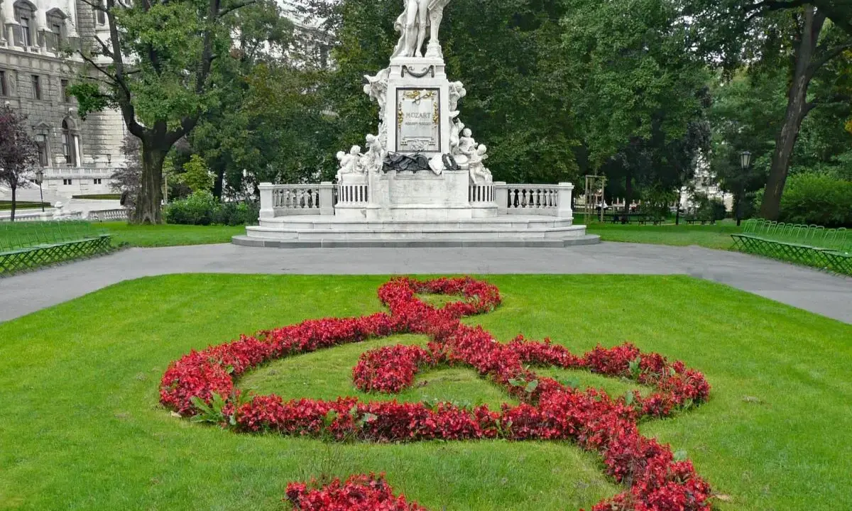 Pomnik Mozarta w Wiedniu, z kluczem wiolinowym ułożonym z czerwonych kwiatów na trawniku.