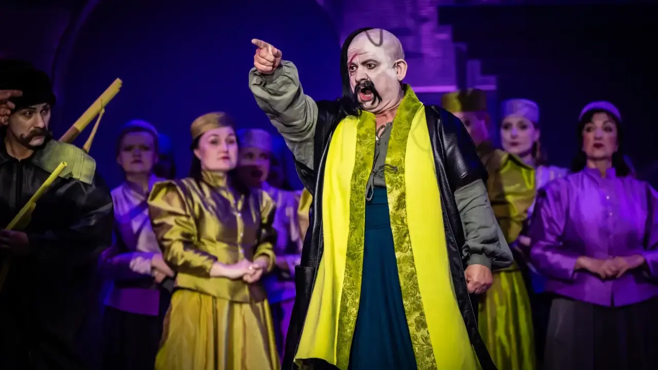 Aktorzy w barwnych strojach na scenie, przypominający postacie z operetki Moniuszki.