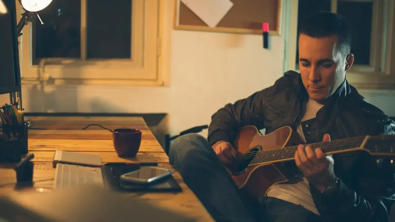 Mężczyzna gra na gitarze, ćwicząc skale gitarowe przy biurku.