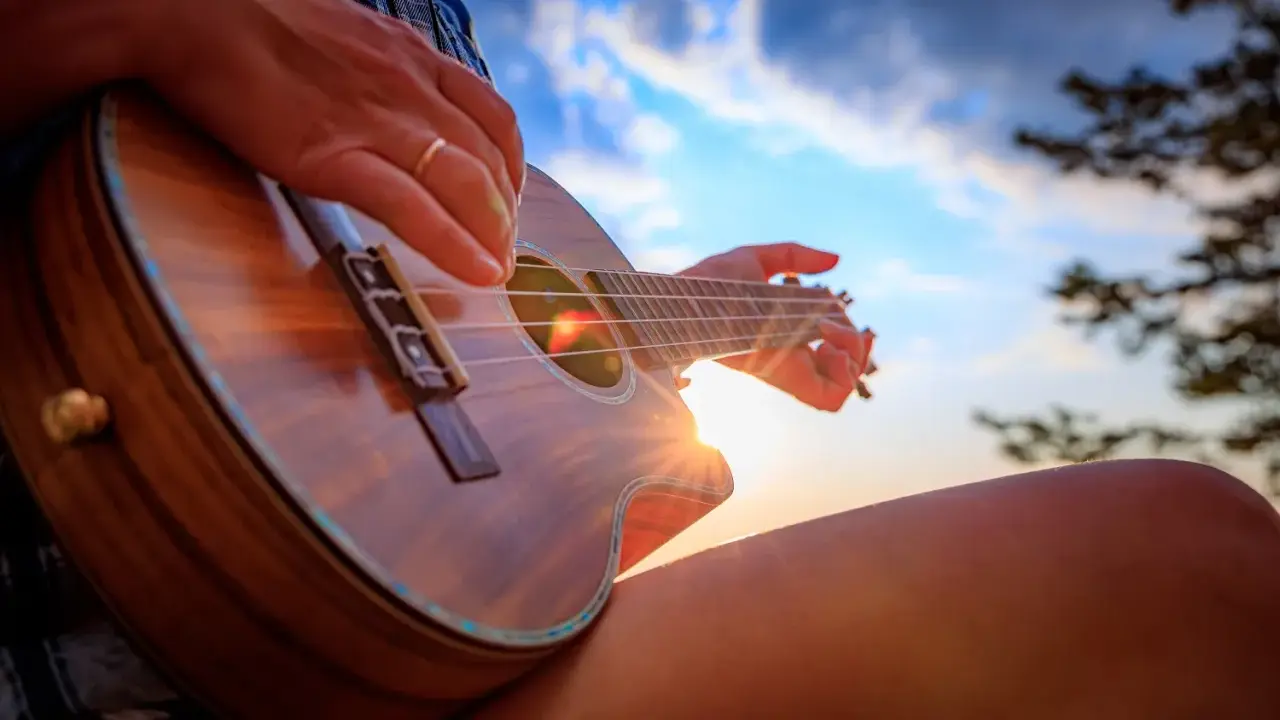 Dłoń z pierścionkiem pokazuje, jak trzymać ukulele, grając przy zachodzącym słońcu.
