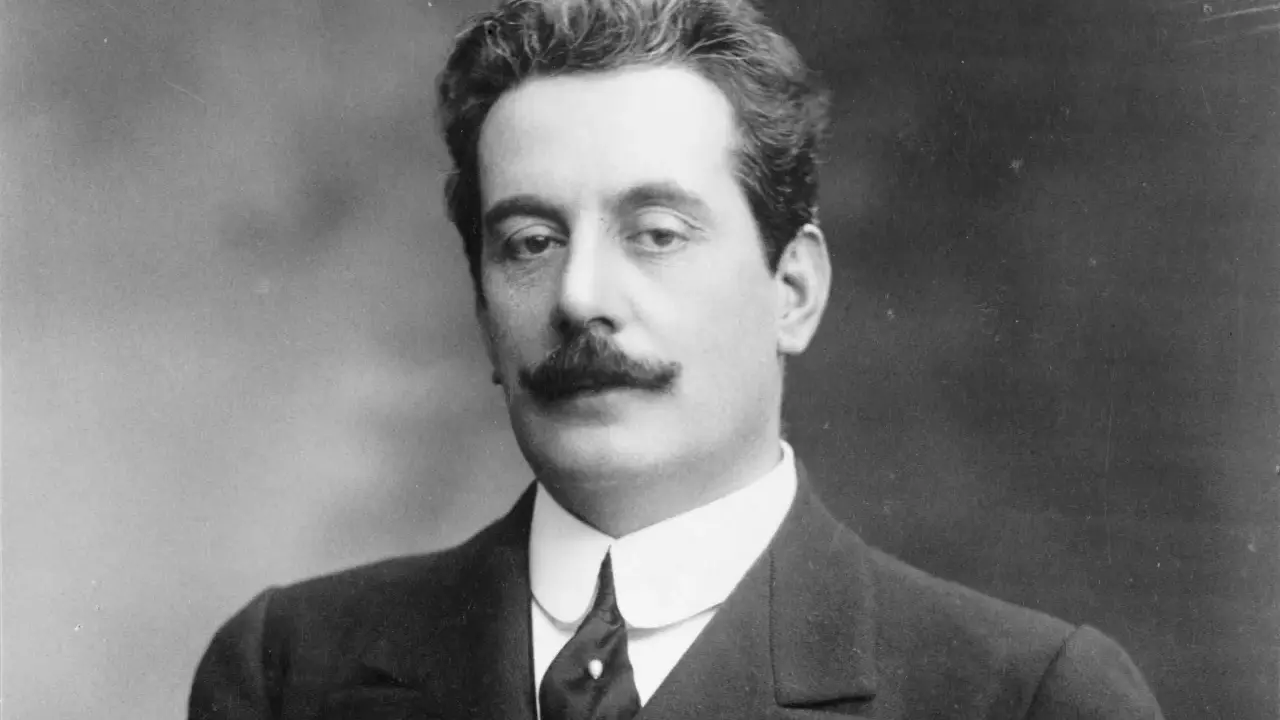 Portret Giacomo Pucciniego, kompozytora operowego, z charakterystycznymi wąsami i w eleganckim garniturze.