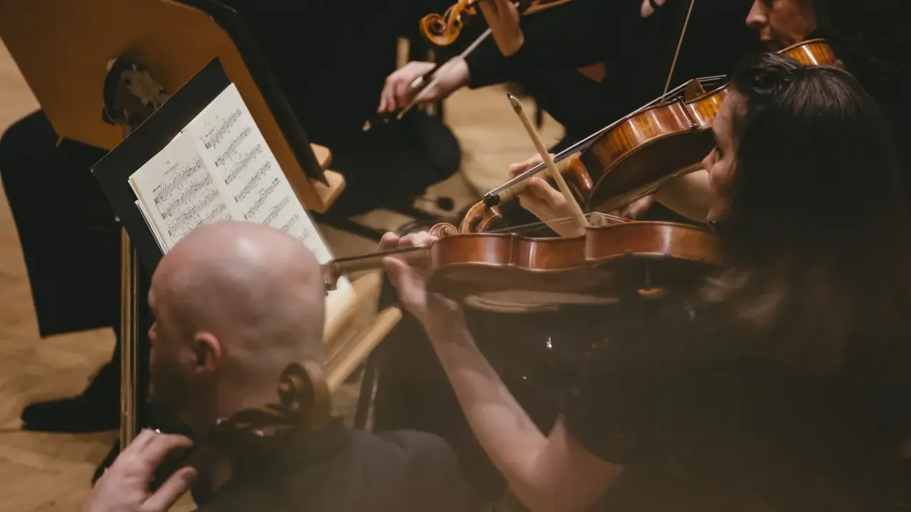 Skupieni muzycy grają na skrzypcach podczas części koncertu bez solisty. Nutki na pulpicie wskazują melodię.