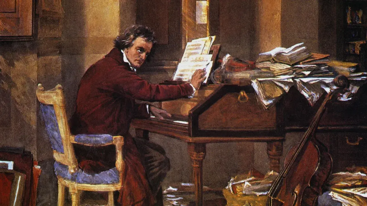 Beethoven, który kompozytor był głuchy, siedzi przy fortepianie, otoczony nutami i książkami.
