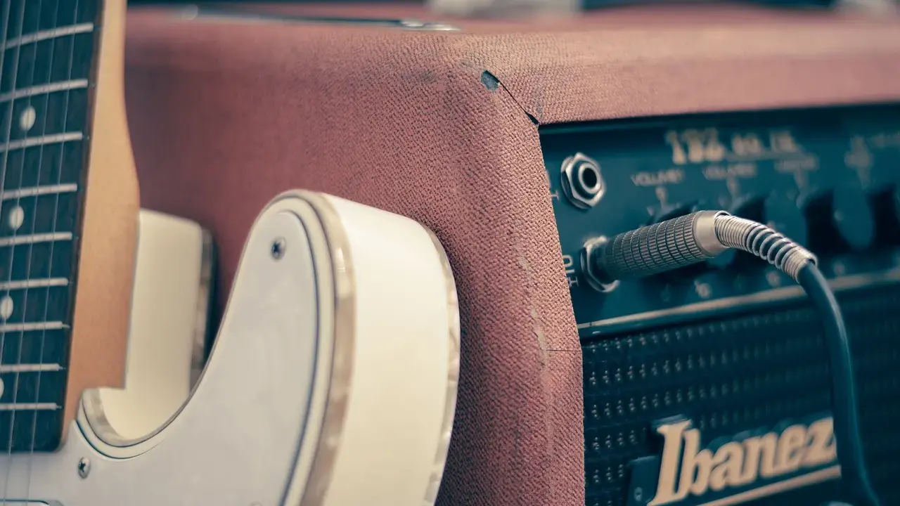 Biała gitara elektryczna podłączona do wzmacniacza Ibanez. Idealny zestaw, by zacząć naukę, jak grać na gitarze elektrycznej.