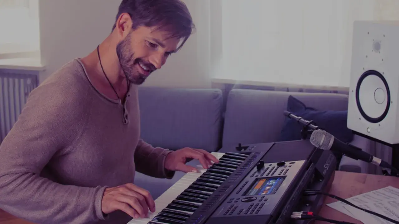 Uśmiechnięty mężczyzna gra na keyboardzie Yamaha, korzystając z aplikacji yamaha flowkey. Obok stoi mikrofon i głośnik.