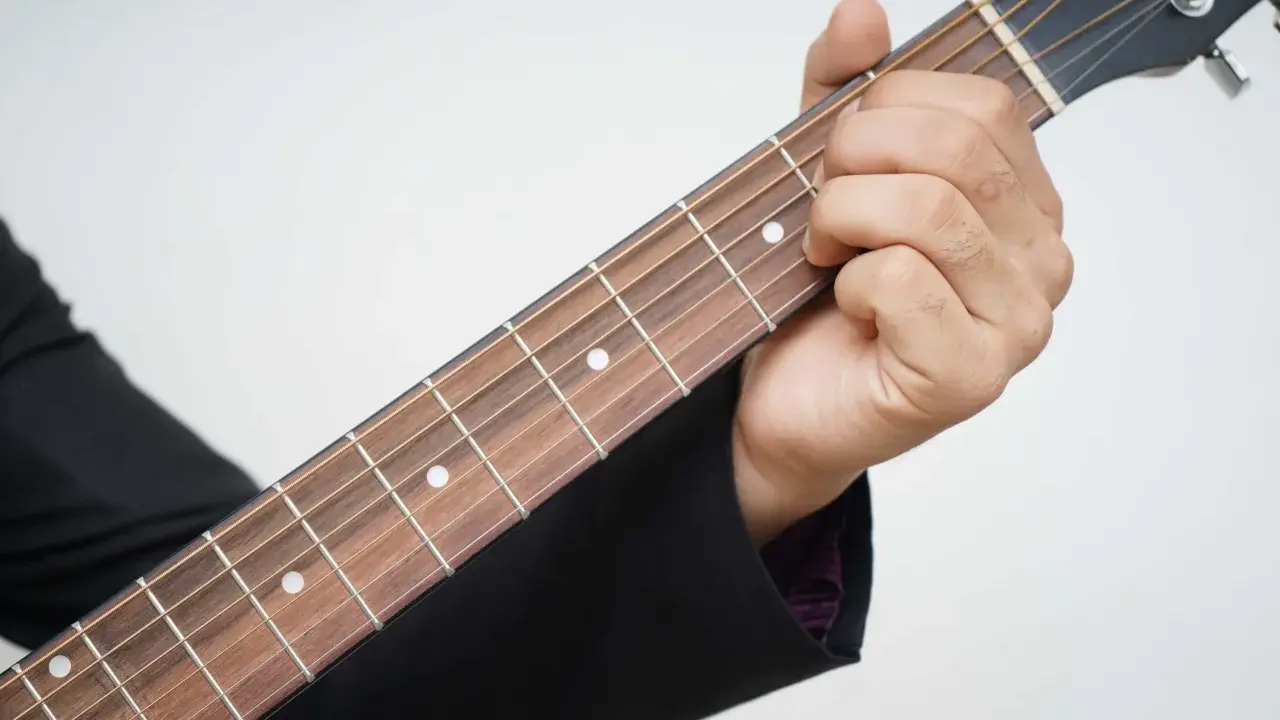 Dłoń dociska struny na gryfie gitary, pokazując pierwszy krok, jak nauczyć się grać na gitarze.