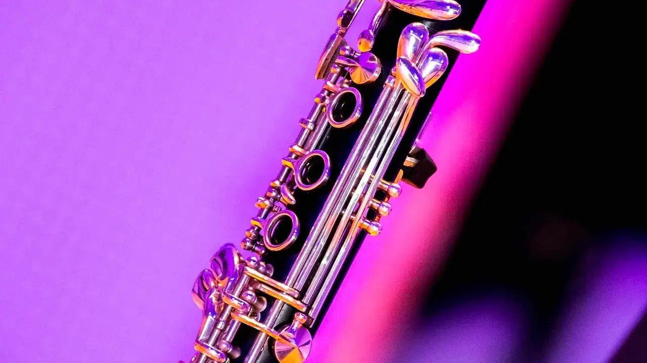 Zbliżenie na klarnet, piękny instrument dęty drewniany, z błyszczącymi klapami na tle fioletowo-różowego światła.