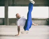 Mężczyzna w białej koszulce i niebieskich spodniach wykonuje akrobatyczny ruch. Czy to może być odpowiedź na pytanie: beatbox co to?
