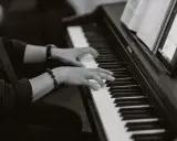 Dłonie grające na pianinie, tworząc improwizowany kierunek w muzyce jazzowej.