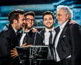 Czterech mężczyzn w garniturach, w tym legendarny tenor, który ma najwyższy głos męski, śmieje się na scenie.