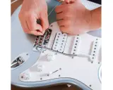 Ręce montują struny do mostka gitary elektrycznej. To ważny krok, jak zrobić gitarę elektryczną, by brzmiała idealnie.