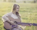Dziewczyna gra na gitarze, tworząc piękny riff. Słońce delikatnie oświetla jej blond włosy i koronkową sukienkę.