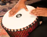 Dłonie grają na djembe, rodzaju bębna o kolorowym korpusie.