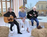 Trzech muzyków gra na gitarach, tworząc muzykę country. W tle stylizowana scenografia z Dzikiego Zachodu.