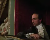 Scena z filmu o Mozarcie. Mężczyzna w stroju z epoki, w loży teatralnej, z widownią w tle.