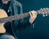 Mężczyzna w skórzanej kurtce gra na gitarze. Akordy układają się w piękną tonację d dur, tworząc melodyjną opowieść.