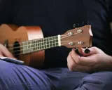 Osoba stroi ukulele, korzystając z aplikacji do nauki gry.