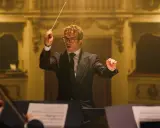 Dyrygent w garniturze prowadzi orkiestrę, tworząc muzykę godną najlepszych polskich kompozytorów muzyki filmowej.