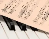 Partytura muzyczna na klawiaturze pianina. Widoczne nuty i klucze, które oddają bogate **cechy muzyki barokowej**.