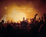 Tłum ludzi z rękami w górze, świętujący koncert. W tle scena z oświetleniem, tworząca atmosferę amerykańskiego stylu w muzyce.