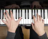 Dłonie grające akordy na pianinie. Muzyka płynie z klawiszy.