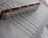 Harmonijka ustna spoczywa na kartach z nutami, gotowa do zagrania melodii.
