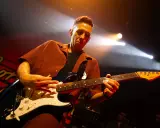 Cory Wong w akcie tworzenia muzyki na scenie, skupiony na grze na gitarze elektrycznej.