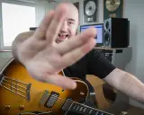 Muzyk z gitarą jazzową, z ręką na pierwszym planie, śpiewa, wyjaśniając, akord co to.
