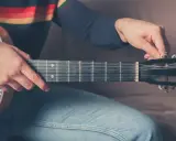 Mężczyzna stroi gitarę 12 strunową, kręcąc kluczem przy główce instrumentu.