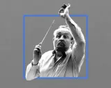 Krzysztof Penderecki, dyrygent z batutą w dłoni, w skupieniu prowadzi orkiestrę.