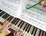 Dziecko uczy się grać na pianinie, ćwicząc nuty z podręcznika. Zielony ołówek wskazuje fragment partytury, co ułatwia naukę gry na instrumentach dla dzieci.