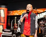 Mężczyzna z mikrofonem, w kurtce z logo Antyradia, na tle instrumentów i scenografii Antyfestu Antyradia.