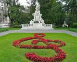 Pomnik Mozarta w Wiedniu, z kluczem wiolinowym ułożonym z czerwonych kwiatów na trawniku.